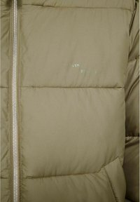 Olivgrön pufferjacka med kviltat mönster, silverfärgad dragkedja och diskret logotyp på bröstet. Slät textur och isolerande vaddering.