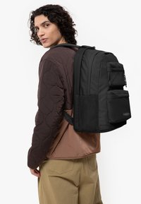 Mochila negra con múltiples bolsillos, hecha de tela resistente, con un diseño elegante, correas ajustables y un bolsillo lateral de malla.