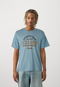 Light blue cotton t-shirt with a round neckline, short sleeves, and a printed graphic featuring "Jack & Jones" and various text details.