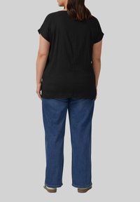 Zwarte, gestructureerde blouse met korte mouwen, gecombineerd met losse blauwe denim jeans. De outfit wordt compleet gemaakt met bruine, platte schoenen.