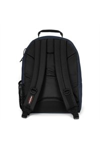 Svart vadderad ryggsäck med justerbara remmar, ett handtag på toppen och en sidficka i mesh. Tyget har en slät yta och en minimalistisk design.