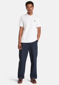 Bílá bavlněná polo košile s krátkým rukávem a malým logem, spárovaná s námořnickými cargo kalhotami s bočními kapsami a volným střihem.