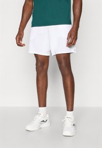Hvite treningsshorts med svart logo, kombinert med hvite joggesko og sokker i knehøyde. Skjorten er grønn og kortermet.