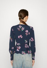 Blusa floreale a maniche lunghe in tessuto blu navale, con fiori rosa e foglie verdi, cintura a peplo e polsini abbottonati.