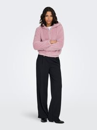 Veste courte rose en tissu duveteux avec capuche, dotée d'une fermeture éclair à l'avant. Assortie à un pantalon noir à jambes larges et des chaussures noires. Design simple.