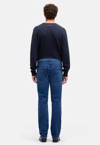 Granatowa koszula z długim rękawem i niebieskie dżinsy. Dżinsy mają prosty krój, tylne kieszenie oraz subtelne detale przeszyć. Strój wygląda swobodnie.