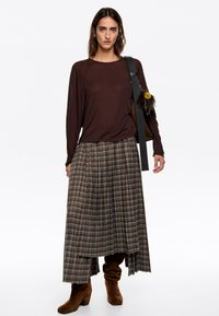 Bruine langemouwen shirt, geruiten maxi rok in aardetonen, bruine enkellaarzen. Rok heeft plooien en een asymmetrische zoom.
