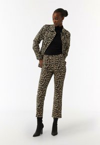 Leopard print jacket and pants set in beige and black, featuring a tailored fit. Black turtleneck underneath, paired with black ankle boots.