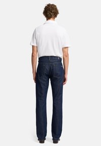 Jeans in denim blu scuro con taglio dritto, abbinati a una polo bianca. Presentano tasche posteriori standard e passanti per cintura.