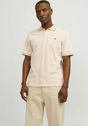 Polo shirt rose clair avec des finitions contrastées vertes et blanches au niveau du col et des manches. Possède un petit emblème sur la poitrine gauche. Manches courtes.