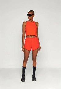 Piros sportos crop top és rövidnadrág szett, laza fazonnal, ujjatlan dizájnnal, sima textúrával, fekete zoknikkal és tornacipőkkel párosítva.