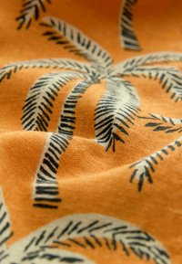 Baumwollstoff mit orangefarbenem Hintergrund, der mit schwarzen Palmenblattmustern verziert ist. Die Textur wirkt weich und leicht zerknittert.