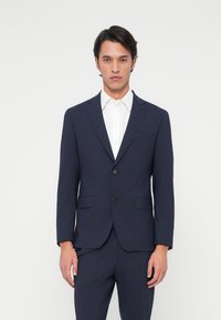 Ναυτικό σακάκι �με κομψή εφαρμογή, κλείσιμο με μονό κουμπί, καπάκια στο λαιμό και τσέπες με καπάκι, συνδυασμένο με λευκό πουκάμισο.