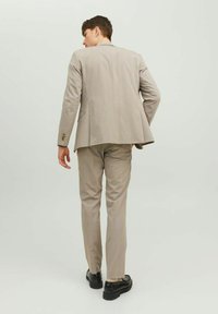 Completo beige a due pezzi con taglio dritto, tessuto strutturato e un delicato motivo a righe sottili. Le scarpe sono nere, con una suola leggermente chunky.