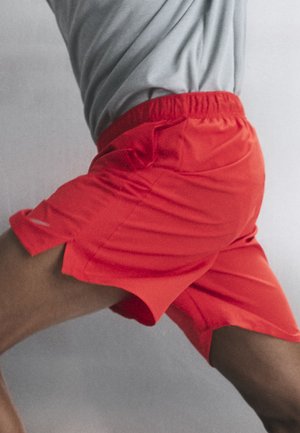 Inimene punastes spordipükstes ja halli särgiga, painutatud jalaga, paistab olevat tegevuses neutraalsel taustal.