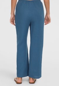 Blue, wide-leg pants made from textured fabric with an elastic waistband, matching sandals visible at the bottom hem.