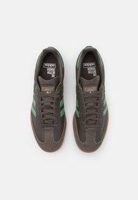 Braune Sneakers mit grünen Streifen, aus Leder und Veloursleder, runde Zehenspitze, flache Schnürsenkel und einer strukturierten Gummisohle. Minimale Markierung an der Zunge.