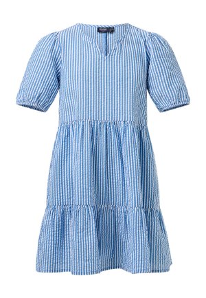 Jeune fille debout, les mains derrière le dos, portant une robe à rayures bleues et blanches et des chaussons roses en peluche.