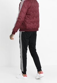 Burgundyröd quiltad jacka med vita ränder, svart elastisk midja och muddar. Svarta byxor med tre vita sidostripor. Vita sneakers med röda accenter.