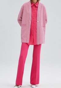 Roze oversized jack met ruitpatroon en zakken, gedragen over een felroze shirt en gecombineerd met roze wijde broekspijpen. Gladde textuur, gedurfde kleur.