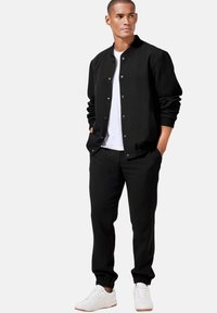 Schwarze Bomberjacke mit Druckknöpfen, kombiniert mit schwarzen Jogginghosen und weißen Turnschuhen. Einfaches, elegantes Design mit elastischen Bündchen.