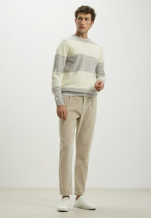 Maglione a maglia a strisce crema e grigie, scollo rotondo, polsini a costine, abbinato a pantaloni beige e sneakers bianche. Texture liscia.