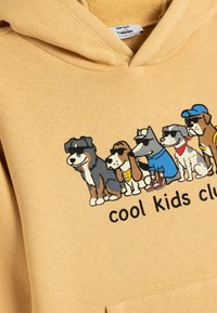 Sudadera de algodón amarillo claro con un gráfico de seis perros de dibujos animados con gafas de sol, con el texto "club de los chicos geniales" abajo.