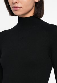 Čierny vrúbkovaný top s vysokým golierom, priliehavým strihom a jemným logom na hrudi. Hladká textúra a bezšvové spracovanie.