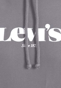 Tissu de sweat à capuche gris avec le texte du logo Levi's blanc partiellement visible sous deux cordons suspendus.