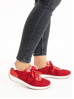 Legs wearing dark gray skinny jeans and red knit sneakers with white soles and red laces on a white background.