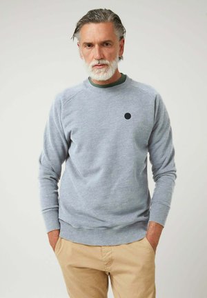 Sudadera gris claro de tela suave con puños acanalados y un cuello redondo, que presenta un pequeño logo de punto negro en el pecho.