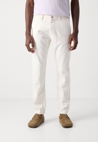 Vita bomullsbyxor med rak passform, med knäppning och framfickor, matchade med bruna mockaskor i slip-on modell.