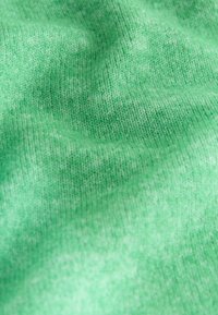 Gros plan d’un tissu tricoté vert doux montrant une texture détaillée et des plis subtils.