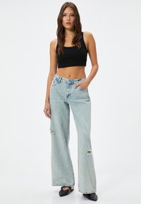 Ljusblå vida jeans med rivna detaljer, hög midja och denimtextur. Kombineras med en svart figurnära cropped top och svarta skor.