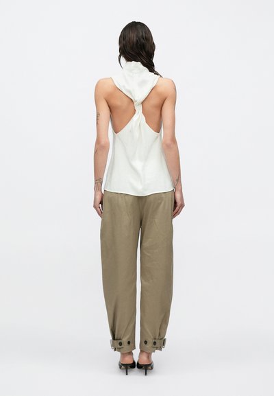 Valge varrukateta topp sõlmitud seljakujundusega, millel on lahtised helepruunid püksid reguleeritavate mansettidega ja mustad kõrge kontsaga kingad.