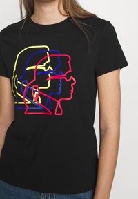 Musta puuvillapaita, jossa on graafinen design limittäin olevista profiileista punaisena, keltaisena ja sinisenä, klassisella pyöreällä kauluksella ja lyhyillä hihoilla.