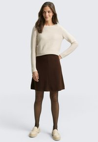 Beige geribbelde trui met lange mouwen gecombineerd met een bruine flared rok. Het model draagt zwarte panty's en beige platform loafers.