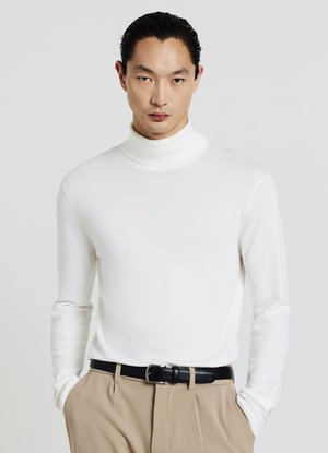 White turtleneck sweater in a smooth fabric, featuring long sleeves and a fitted design. Worn with beige trousers and a black belt.