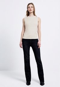 Top beige senza maniche con texture a coste, abbinato a jeans dritti scuri e stivali neri alla caviglia. Design semplice con accenti minimi.