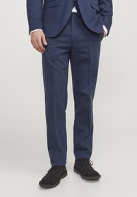 Pantaloni bleumarin dintr-un material texturat, cu croială dreaptă, buzunare frontale și purtați cu pantofi negri din suede.