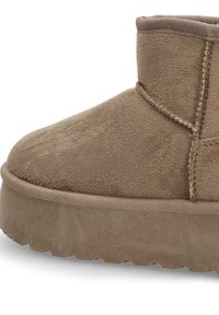 Botín de ante color beige con punta redonda, parte superior texturizada y suela de goma con un patrón de zigzag en el borde.