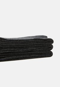 Schwarze Socken, ordentlich gestapelt, aus weichem, strukturiertem Material mit Rippendesign. Abgerundete Spitzen mit gleichmäßigen Nahtdetails entlang der Kanten.