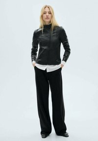 Black leather jacket with a high neck and front zipper, worn over a white shirt and paired with black wide-leg pants. Smooth texture.