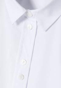 Camicia bianca con bottone, caratterizzata da un colletto classico, realizzata in tessuto morbido, con bottoni visibili e cuciture ben rifinite.