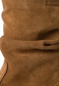 Botas de ante marrón hasta la rodilla con una textura suave, detalles de costura y un diseño holgado con la parte superior ligeramente curvada.