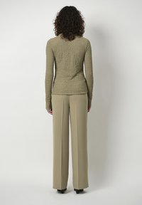 Beige strukturierte Langarmbluse mit figurbetontem Bund, kombiniert mit weit geschnittenen, hellbeigen Hose. Einfaches Design, keine sichtbaren Verzierungen.
