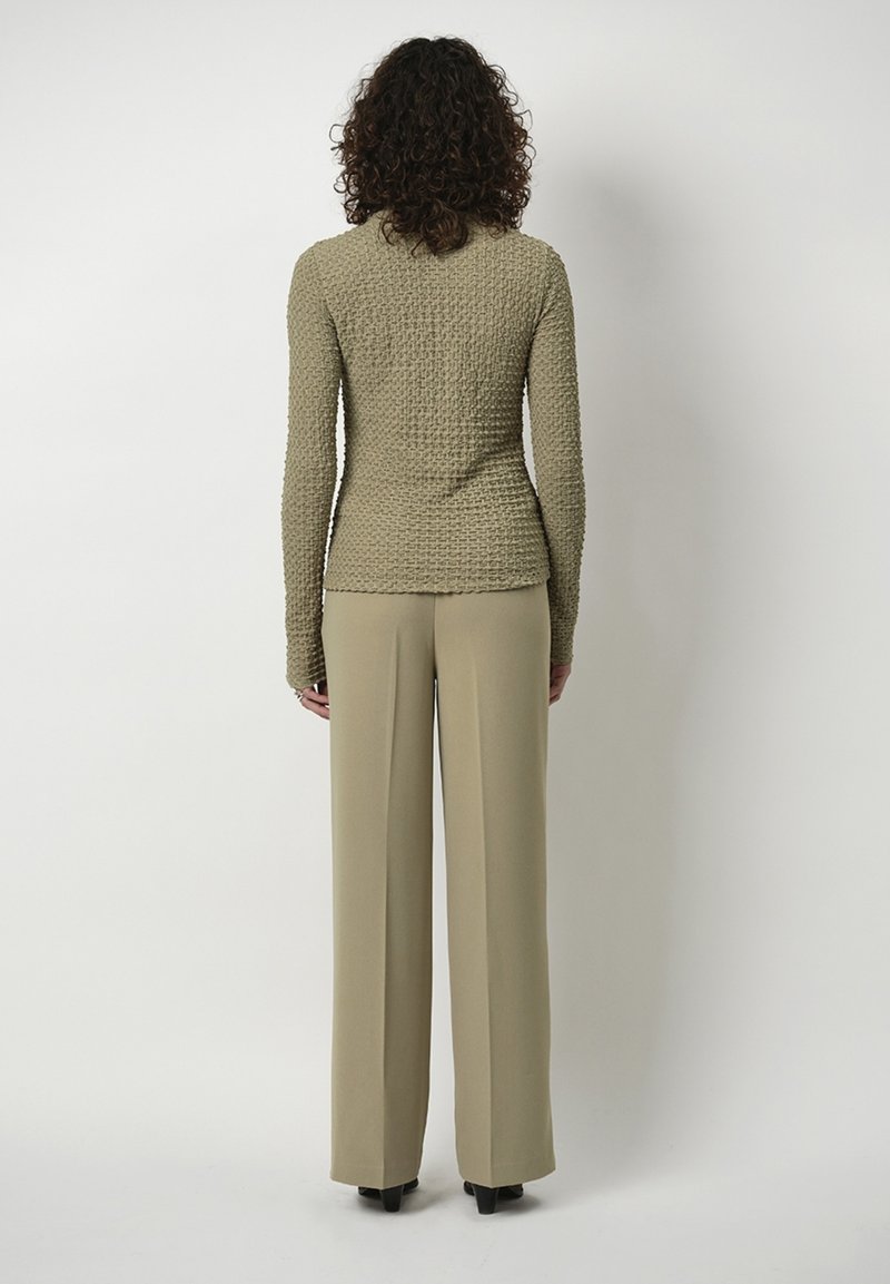Beige strukturierte Langarmbluse mit figurbetontem Bund, kombiniert mit weit geschnittenen, hellbeigen Hose. Einfaches Design, keine sichtbaren Verzierungen.