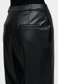 Τα μαύρα δερμάτινα παντελόνια διαθέτουν λεία υφή, στενή εφαρμογή και πίσω τσέπη με επίπεδη ραφή. Περιλαμβάνουν θηλιές για ζώνη και διακοσμητικά στοιχεία από μέταλλο.