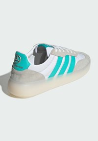 Sneaker featuring a white textile upper with grey suede accents and teal stripes. Equipped with a semi-transparent sole and branded heel detail.