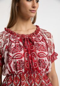 Rød bluse med blomsterprint, udvalg med en sammensnøret halsudskæring, korte flæseærmer og en indsnævret talje i let, gennemsigtig stof.